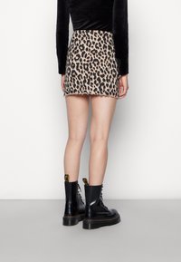 Tan en zwart panterprint minirok met golvende zoom, gecombineerd met zwarte veterschoenen met een legerstijl en gele accenten.