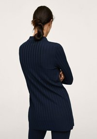 Túnica de manga larga de canalé en color marino con cuello, que presenta un corte recto y aberturas laterales, exhibiendo una textura vertical y una tela suave.