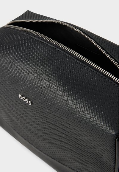 Gros plan sur un sac BOSS noir texturé, avec une fermeture éclair argentée partiellement ouverte et un petit logo en métal.