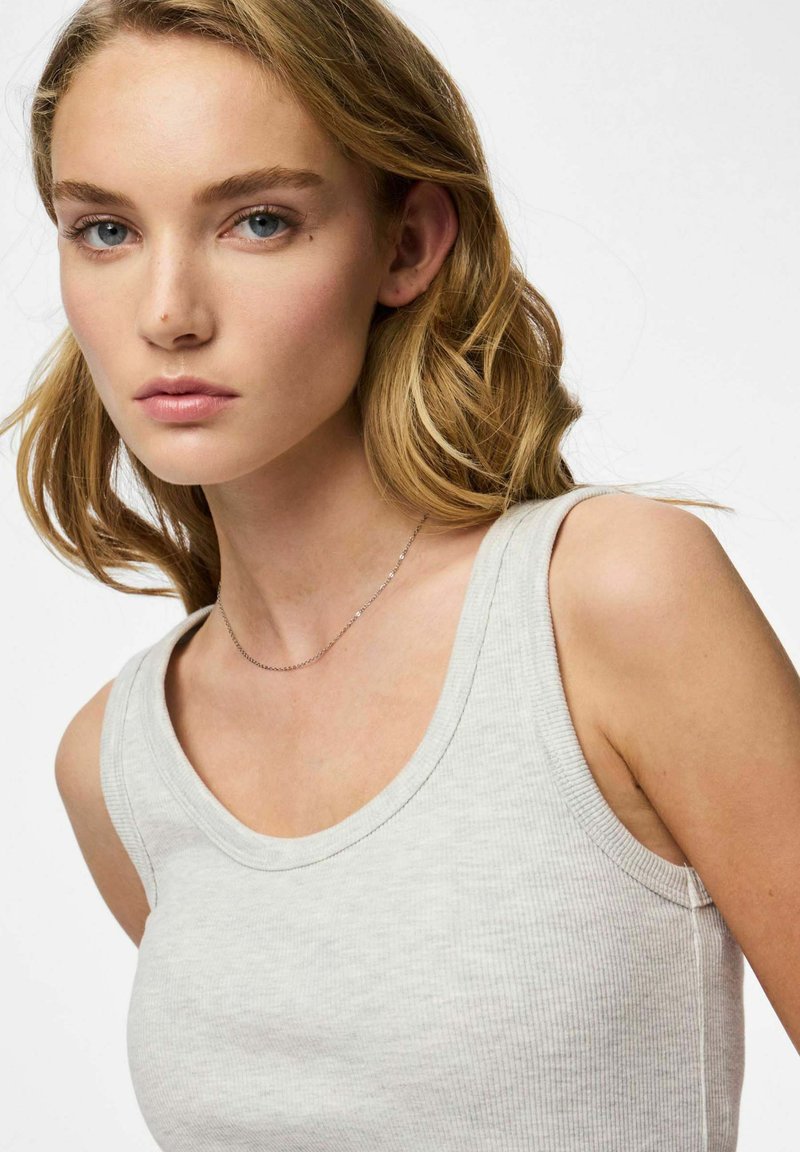 Débardeur gris clair à côteaux avec un décolleté arrondi, montrant une texture lisse. Un fin collier en argent souligne discrètement le décolleté.