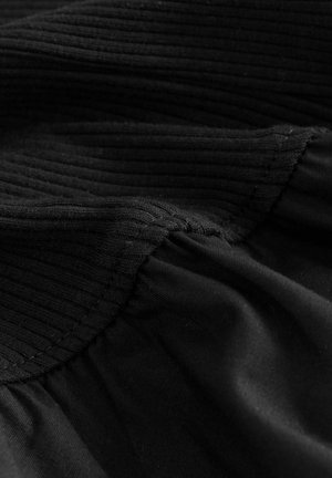 Material negru cu o textură canelată, cu secțiuni netede și cusături vizibile la îmbinări, evidențiind variații în grosime și cădere.