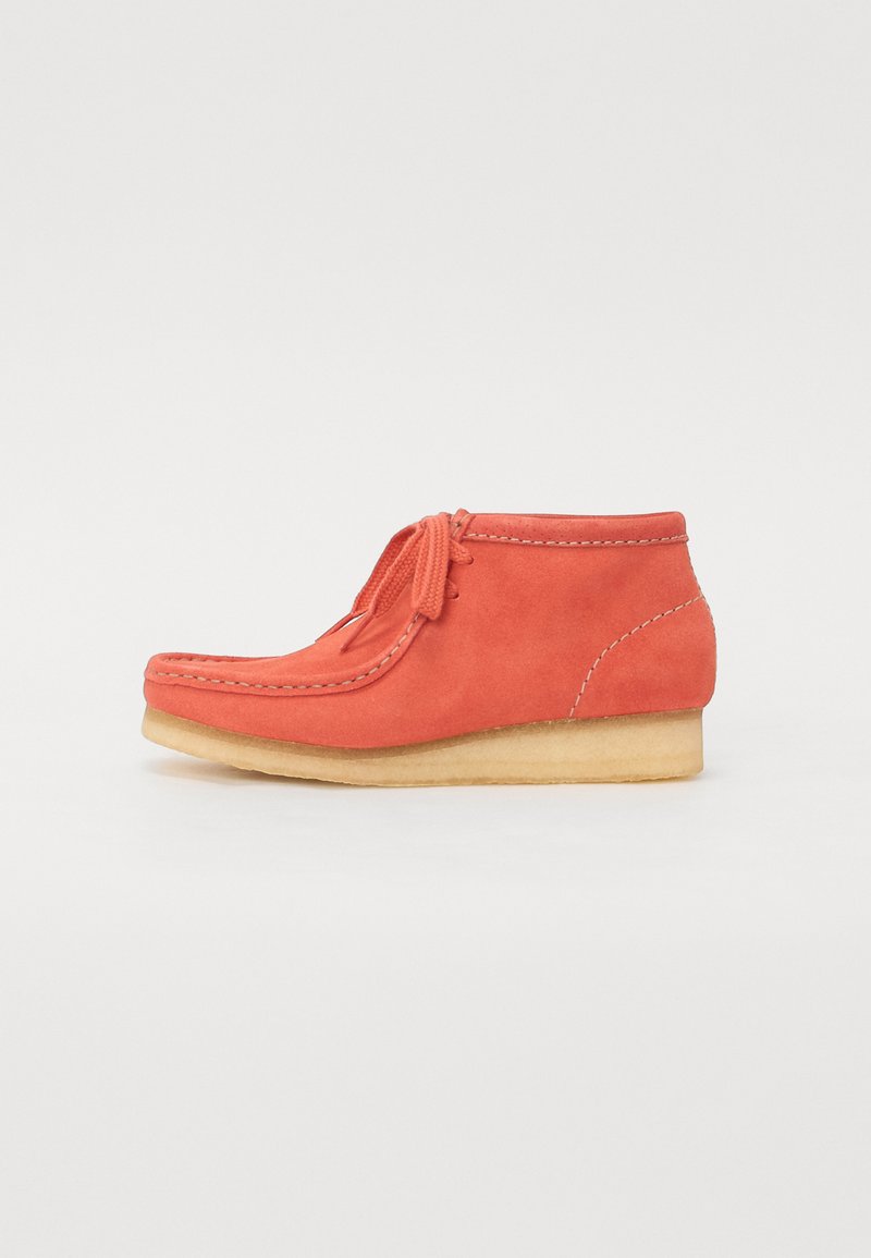 Botín de ante en un vibrante color coral con un acabado texturizado, que presenta una punta redonda, cordones en la parte delantera y una suela de goma de color natural y baja.