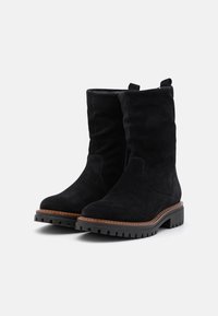 Botines de ante negros con suela gruesa y estriada, detalles cosidos a lo largo del borde y lengüetas en la parte superior para un fácil calzado.