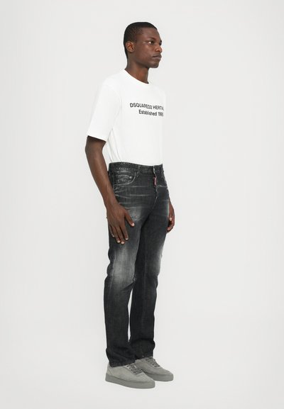 Jeans de mezclilla negra con ajuste Slim, textura desgastada y costuras en contraste, combinados con una camiseta de manga corta blanca con texto negro.