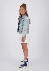 Jeansjakke med farverige lapper, hvid broderi kjole og marineblå høj-top sneakers. Har krøllet hår stylet med en knold.