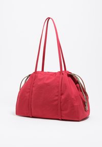 Borsa di stoffa rossa con forma arrotondata, due lunghe cinghie e chiusura con cordoncino. Presenta dettagli a contrasto marroni e superficie teksturizzata.
