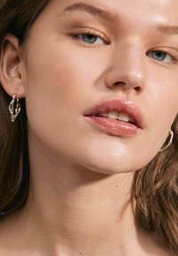 Orecchini a cerchio in argento con un design organico e intrecciato. Il modello ha una carnagione chiara e un trucco naturale.