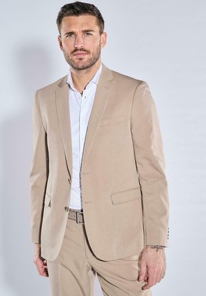 Beige suit with a two-button jacket and notch lapels, paired with a white dress shirt. Features a fitted design and subtle sheen.
