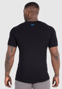 Camiseta ajustada de manga corta negra hecha de tela elástica. Presenta un logo azul en la parte posterior del cuello y puños acanalados. Textura suave.