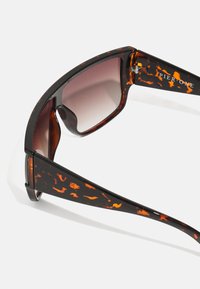 Gafas de sol con un patrón de carey, montura marrón oscuro, lentes con degradado y brazos de marca. Presentan ángulos elegantes y un acabado brillante.