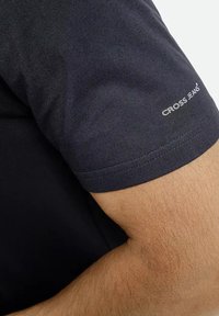 Czarna bawełniana koszulka z krótkim rękawem, z prostym wzorem i białym logo „CROSS JEANS” nadrukowanym na rękawie. Miękka w dotyku.