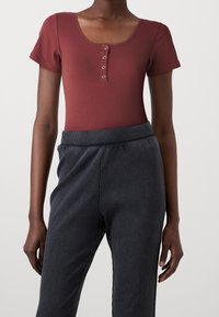 Ribbad bordeaux bodysuit med rundad halsringning, korta ärmar och fem knappar fram. Parat med mörkgrå ribbade, högmidjade byxor.