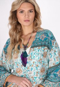Kimono fluido e floreale in azzurro con accenti arancioni e verdi, caratterizzato da un design a fantasia e maniche ampie. Gli accessori includono una collana di perline.