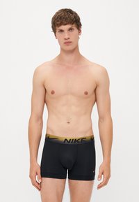 Fekete boxer alsónadrág arany Nike logóval a derékon. Az anyaga sima, rugalmas és kényelmes illeszkedésű.