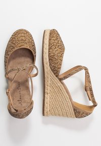 Cuñas con parte superior de tela bronceada decorada con cuentas doradas y marrones. Suela de yute estilo esparto y detalles de correa en el tobillo.
