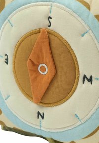 Iránytű formájú díszpárna puha anyagból, bézs és világoskék árnyalatokkal, hímzett irányokkal és strukturált narancssárga iránytűtűvel.