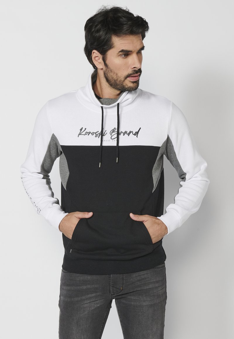 Felpa con cappuccio bianca e nera con dettagli grigi, dotata di tasca frontale e logo. Materiale morbido con blocchi di colore a contrasto.
