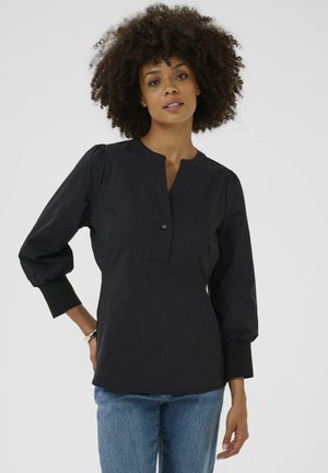 Blusa negra con cuello henley, mangas abullonadas y cierre de botones. Tela suave, corte estructurado y un dobladillo que cae a la altura de las caderas.