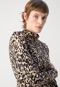 Leopardo rašto ilgomis rankovėmis viršus su aukštu apykakle. Minkšta medžiaga, prigludusi siluetas, išryškintos ryškios juodos dėmės ant smėlio spalvos fono.