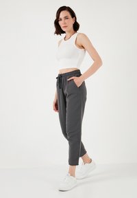Grijze katoenen joggers met een trekkoord in de taille, zijzakken en geknoopte enkels, gecombineerd met een witte geribbelde crop top en witte sneakers.