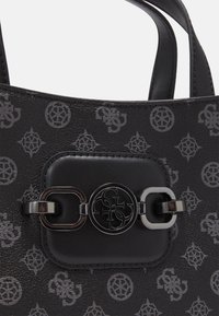 Sac à main noir avec imprimé logo à motif, doté d'une plaque centrale métallique avec le logo Guess et de doubles poignées.