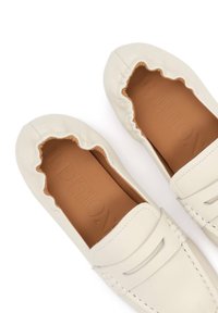 Mocassins loafers en cuir couleur crème avec bords festonnés élastiqués et semelles intérieures tan embossées de texte.