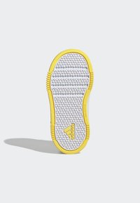 Suela de zapatilla blanca con una superficie texturizada, que presenta un borde de goma amarilla y un logo de Adidas en relieve cerca del talón.