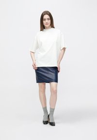 Hvid bomulds oversized t-shirt kombineret med en navy læder mini nederdel. Grå ankelsokker og sorte høje hæle fuldender outfittet.