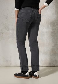 Jeans de mezclilla gris con corte recto, con puños enrollados que tienen un acento estampado. Llevados con zapatillas negras, con bolsillos laterales visibles.