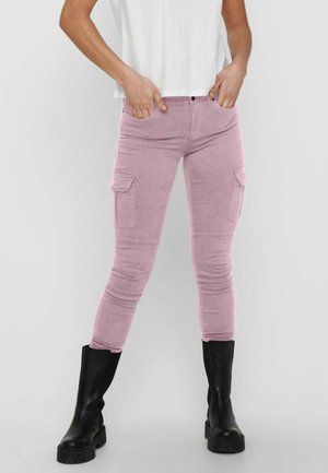 Pantalons cargo roses avec une coupe slim, dotés de deux poches latérales et d'une texture douce. Associés à des bottines noires et un haut blanc.