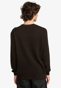 Dunkelbrauner Pullover aus weichem Strickstoff mit rundem Halsausschnitt, langen Ärmeln und lockerer Passform. Sanfte Textur mit gerippten Bündchen.
