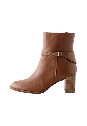 Bottine en cuir marron avec un talon bloc et une sangle décorative avec un détail de boucle en or.