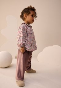 Pasztell színű, virágmintás hosszú ujjú ing, bordázott levendulalila nadrággal és bézs klumpával párosítva, kerek nyakkivágással és kényelmes szabással.