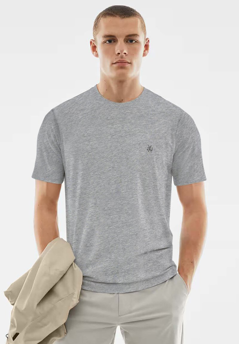 Graues T-Shirt mit kurzen Ärmeln aus weichem Stoff, Rundhalsausschnitt und kleinem schwarzem Logo auf der Brust, getragen von einem Modell, das eine Jacke hält.