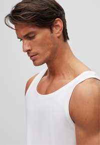Débardeur blanc en coton. Doté d'un col rond et de large bretelles. Texture lisse, design ajusté. Couture soignée.