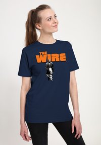 Marinblå t-shirt med kort ärm som har ett grafiskt tryck av en karaktär från "The Wire" och fet orange text. Mjuk bomullsmaterial, avslappnad passform.