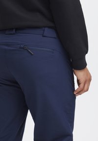 Námořnické modré kalhoty s hladkou texturou, s kapsou na zip na zadní straně a elegantním designem. Pas je plochý a nezdobený.