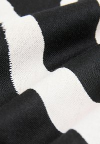 Tissu rayé noir et blanc avec des rayures larges alternées, affichant une texture douce et un aspect tissé. Les bords semblent finis.