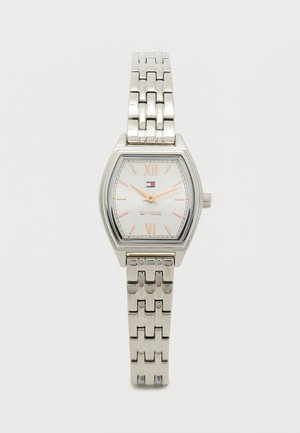 Srebrny metalowy zegarek o kwadratowej kopercie, z białą teksturowaną tarczą wyświetlającą cyfry rzymskie oraz bransoletą z ogniw. Posiada logo.