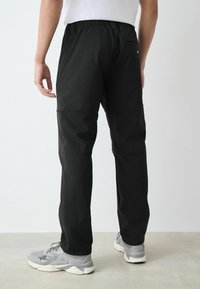 Schwarze leichte Hose mit elastischem Bund, zweifarbigem Design und Seitentaschen. Strukturierter Stoff mit glatter Oberfläche.