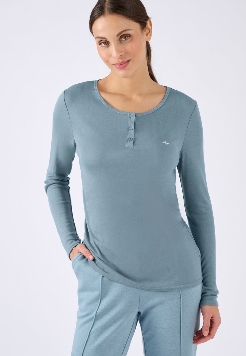 Maglietta azzurra a maniche lunghe con scollatura rotonda, dotata di tre bottoni nella parte anteriore e di un tessuto morbido e strutturato.