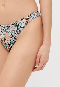 Bikiniunderdel med blommönster som har en svart bakgrund med flerfärgade blommor, medelhög design och mjuk textur. Detaljer inkluderar sidodetaljer.