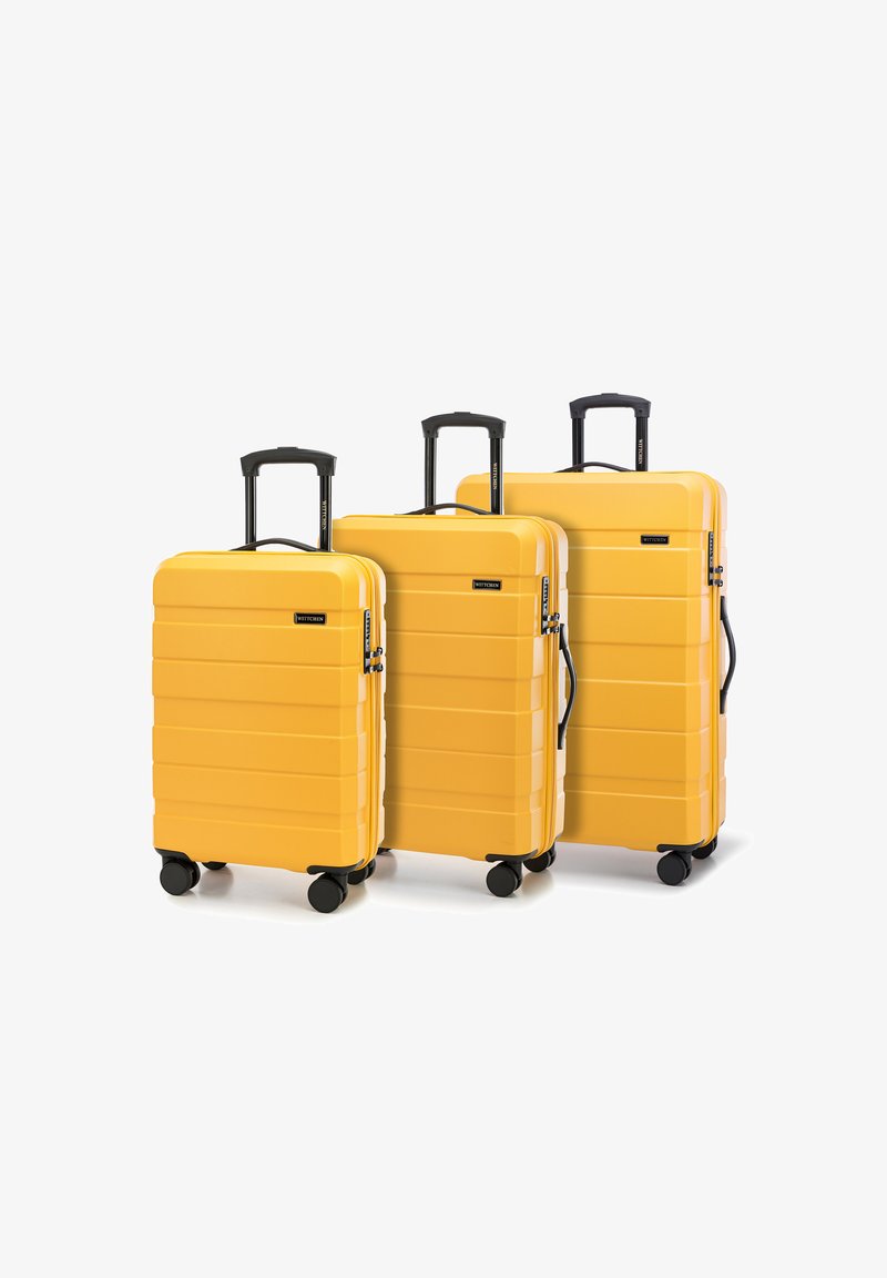 Tři žluté tvrdé kufry různých velikostí. Texturovaný povrch s horizontálními drážkami, černá kolečka a teleskopické rukojeti.