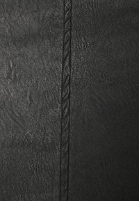 Czarna teksturowana skóra z wyraźnym szwem. Powierzchnia ma subtelny wzór ziarna, o gładkim i lekko błyszczącym wykończeniu.