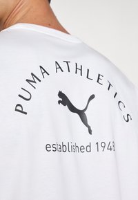 Hvid bomulds T-shirt med "PUMA ATHLETICS" og et sort puma-logo. Inkluderer "etableret 1948" i sort tekst. Rund halsudskæring, korte ærmer.