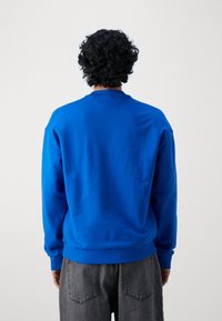 Sudadera azul de cuello redondo con un acabado texturizado, puños y dobladillo de canalé. Diseño sencillo, sin logotipos ni adornos prominentes.