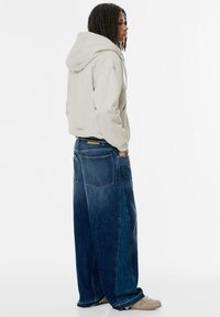 Lys grå hættetr�øje med en frontlomme, parret med brede mørkeblå denim jeans med to baglommer og frayed kantdetaljer.