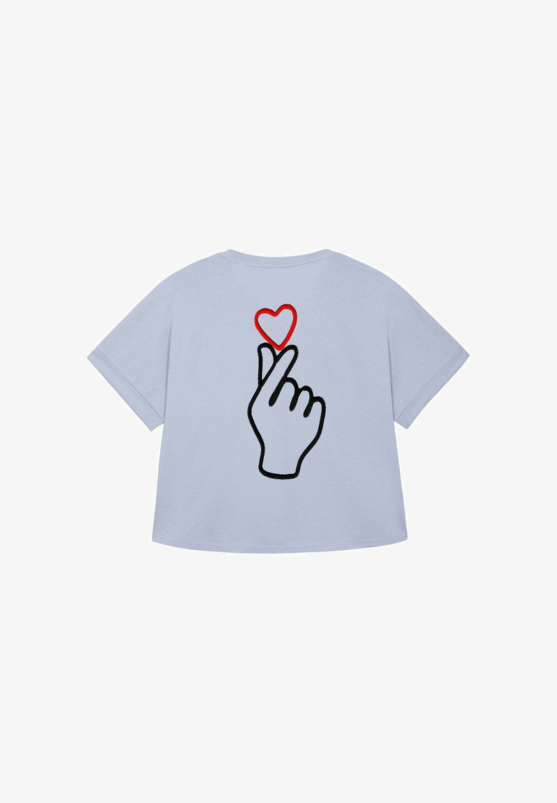 Lichtblauw T-shirt met een afbeelding van een hand die een "vinger hart" gebaar maakt boven een rood hart. Casual en speelse ontwerp.