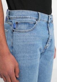 Jasnoniebieskie jeansy z denimu o klasycznym kroju, z talią na wysokości środka, pięcioma kieszeniami oraz niebieską metką z logo na tylnej części pasa.