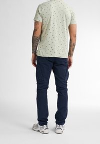 Světle zelená košile s malými černými vzory, doplněná tmavě námořnickými cargo kalhotami. Oblečení doplňují bílé sportovní boty.